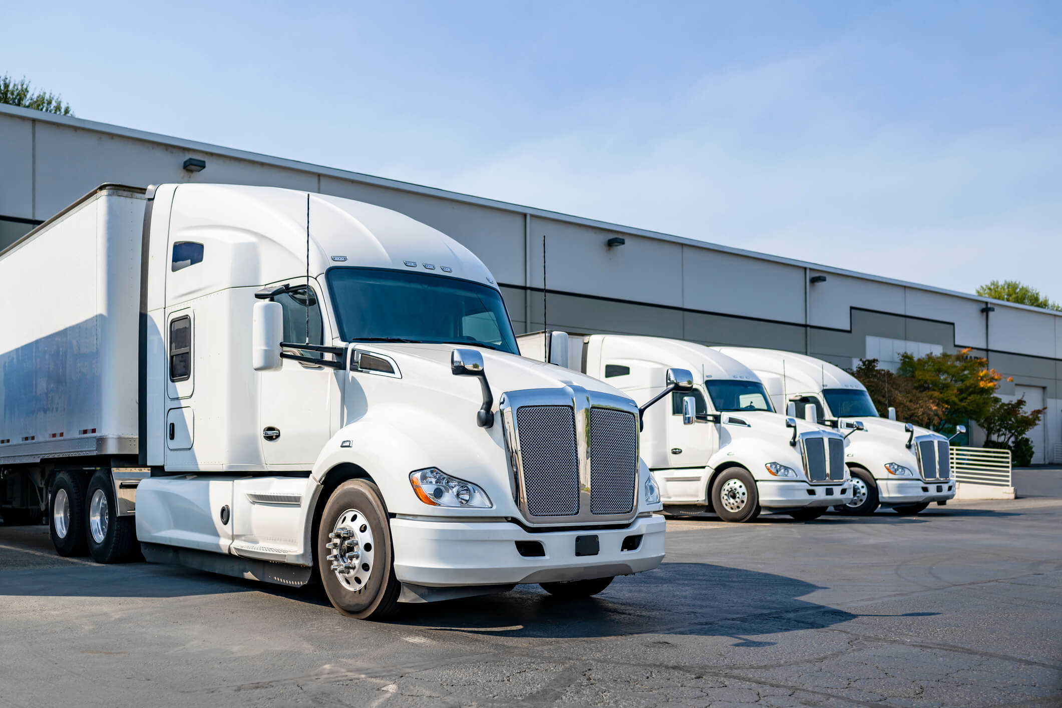 Three white semi-trucks parked at warehouse.