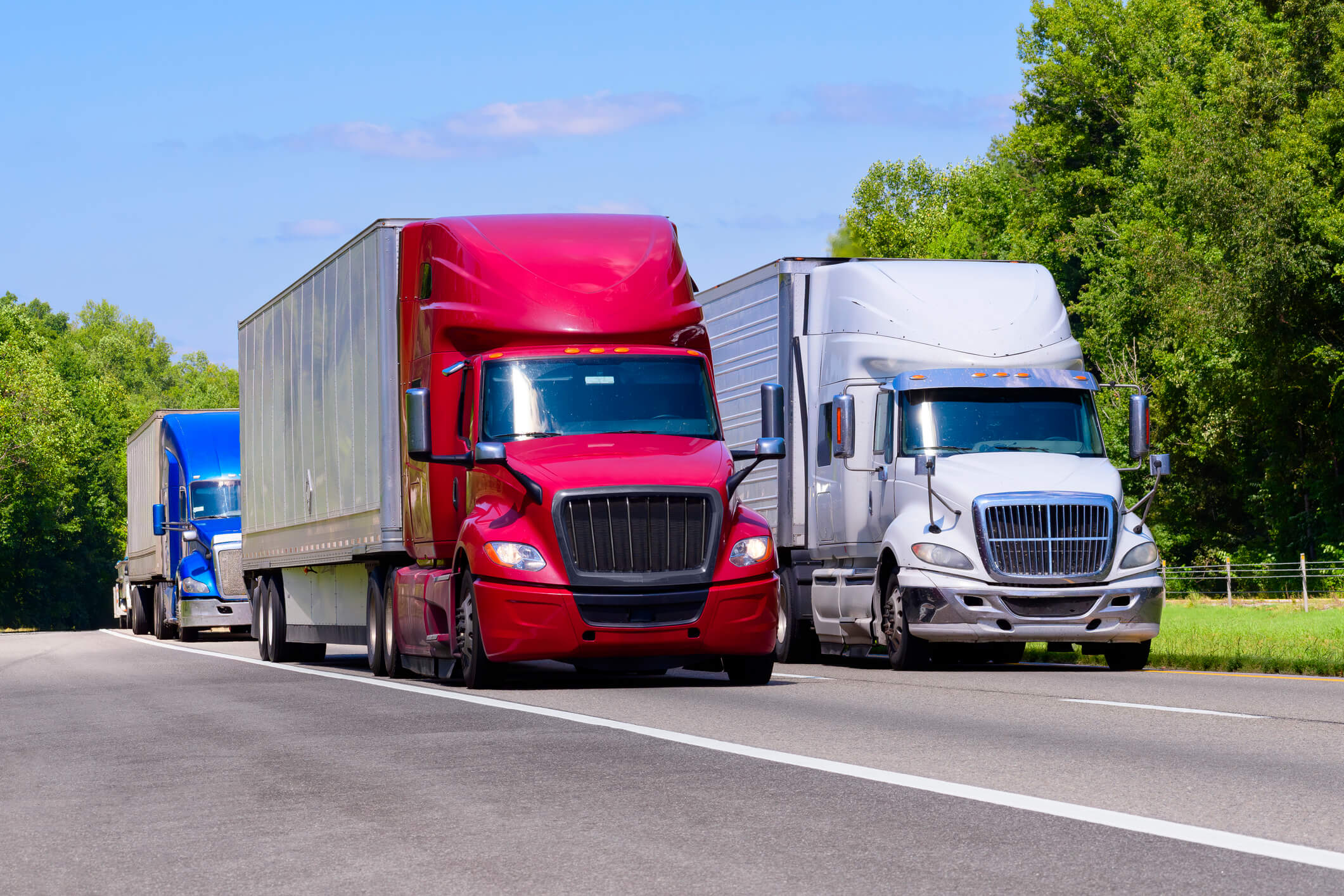 Three semi-trucks driving on highway.